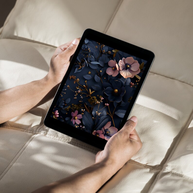 May include: A person is holding a tablet displaying a floral wallpaper with pink and blue flowers on a dark blue background.