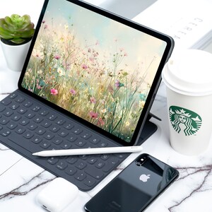 May include: A black iPad with a floral wallpaper, a black keyboard, a white stylus, a black iPhone, and a white coffee cup with a green Starbucks logo.