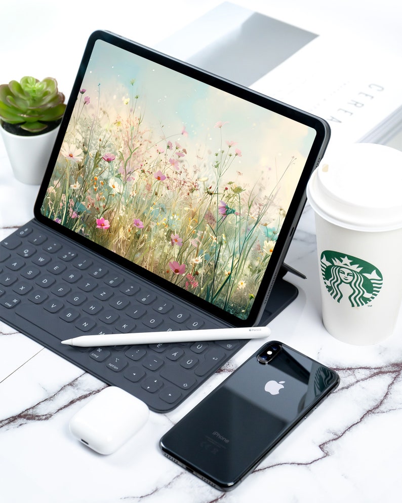May include: A black iPad with a floral wallpaper, a black keyboard, a white stylus, a black iPhone, and a white coffee cup with a green Starbucks logo.