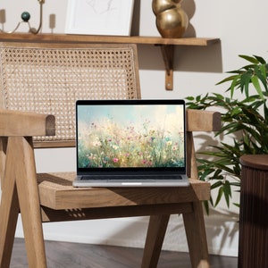 May include: A silver laptop computer with a floral wallpaper on the screen sits on a wooden chair with a woven seat. The chair is in front of a white wall with a wooden shelf above it.