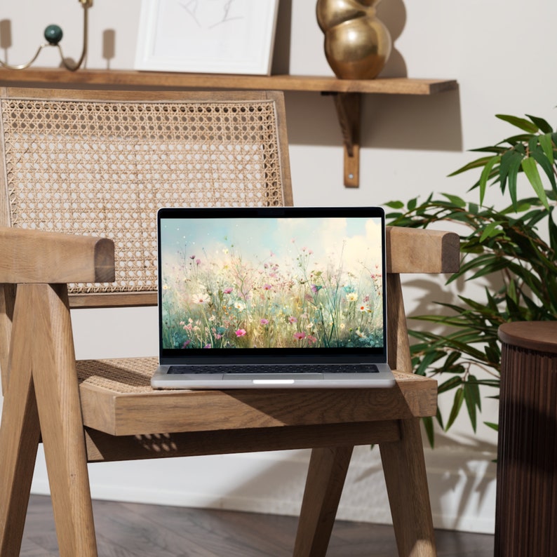 May include: A silver laptop computer with a floral wallpaper on the screen sits on a wooden chair with a woven seat. The chair is in front of a white wall with a wooden shelf above it.