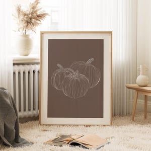 May include: A framed print with a brown background and a white line drawing of three pumpkins.