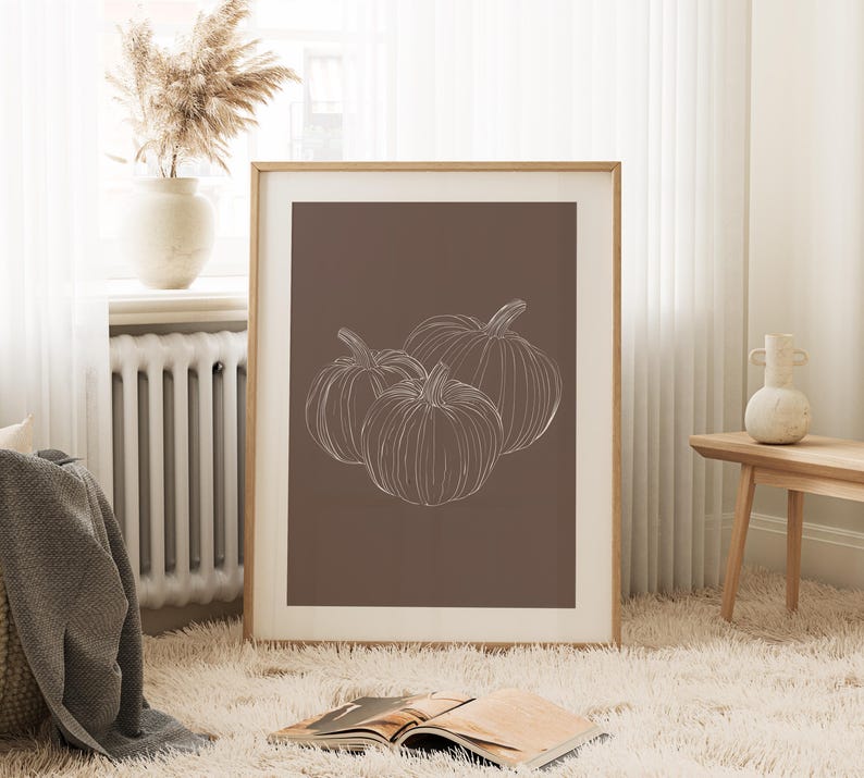 May include: A framed print with a brown background and a white line drawing of three pumpkins.