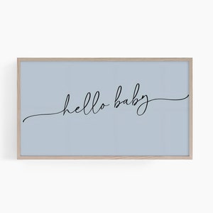 May include: A framed print with a light blue background and the words "hello baby" in elegant black script. The frame is a light wood color, and the overall design is minimalist and modern.