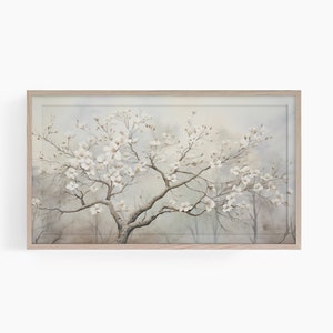 May include: A framed watercolor print of a flowering tree with white blossoms. The artwork features a muted color palette of gray, beige, and white, with a light wood frame. The tree's branches are filled with delicate flowers.