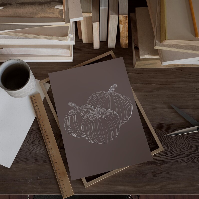 May include: A framed print with a minimalist line drawing of three pumpkins on a brown background.