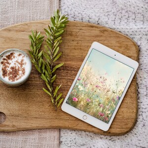 May include: A wooden cutting board with a cup of coffee, a tablet with a floral screen saver, and a sprig of green leaves.