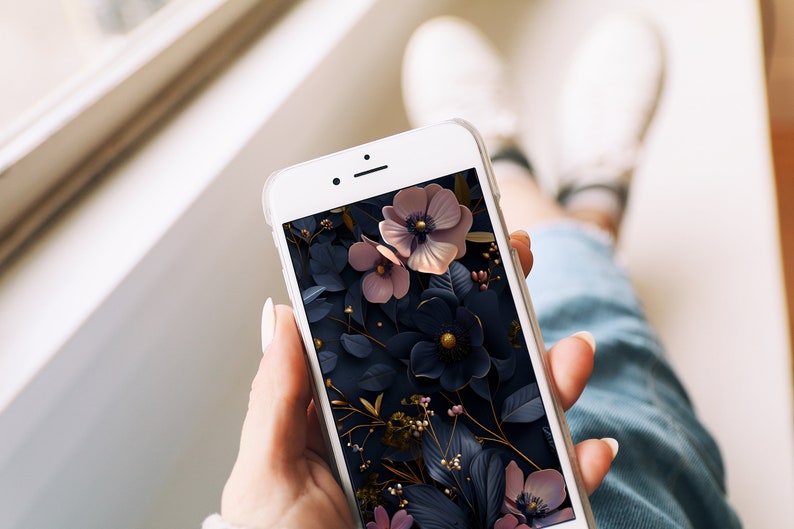 May include: A white smartphone with a floral wallpaper. The wallpaper features pink and blue flowers with gold accents on a dark background.