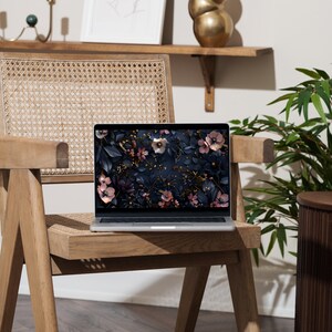 May include: A laptop computer with a floral wallpaper on the screen sits on a wooden chair with a woven cane seat. The chair is in front of a wall with a shelf and a vase.