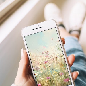 May include: A white smartphone with a floral wallpaper. The wallpaper features a field of pink and white flowers with a soft, blurred background.
