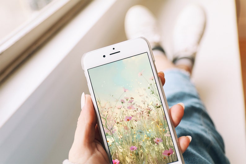 May include: A white smartphone with a floral wallpaper. The wallpaper features a field of pink and white flowers with a soft, blurred background.