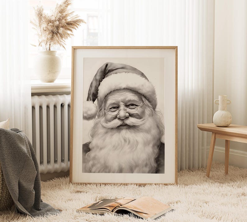 May include: A framed black and white portrait of Santa Claus. The image features a detailed depiction of Santa's face, with a long white beard, round glasses, and a traditional hat. The artwork is displayed in a light-colored wooden frame, suitable for holiday decor.