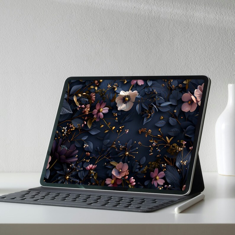 May include: A tablet computer with a dark blue background and a floral pattern in shades of pink, white, and gold. The tablet is on a white surface with a black keyboard and a white stylus.