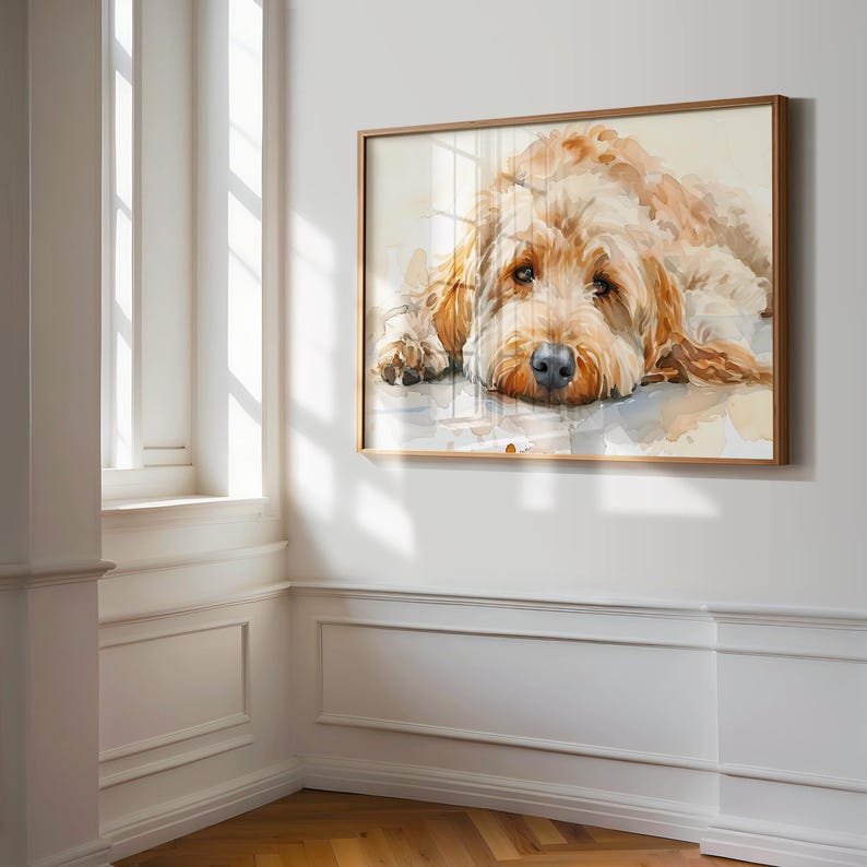 May include: A watercolor painting of a golden doodle dog lying down with its head resting on its paws. The dog has a brown nose and brown eyes. The painting is framed in a light brown wood frame.