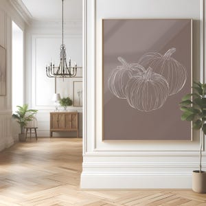 May include: A digital art print featuring a minimalist line drawing of three pumpkins on a light brown background.