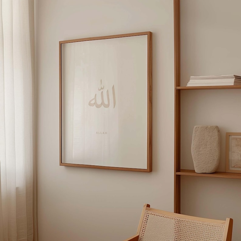 May include: A framed print with a beige background and the Arabic word "Allah" written in a light brown colour. The word "Allah" is written in English below the Arabic word.