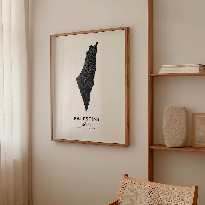 Op de afbeelding: Een zwart-witte kaart van Palestina met het woord "Palestine" en het Arabische woord voor Palestina eronder. De kaart is ingelijst in een licht houten lijst en hangt aan een witte muur.