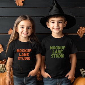 Könnte beinhalten: Zwei Kinder tragen schwarze T-Shirts mit dem Text "Mockup Lane Studio" in verschiedenen Farben. Das Mädchen trägt ein rot-oranges Design, der Junge ein grün-oranges Design. Sie stehen vor einem dunklen Holzhintergrund mit Herbstblättern.