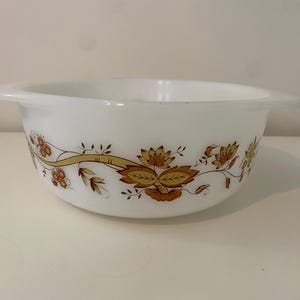 May include: White glass mixing bowl with a floral design in shades of brown and gold. The bowl has two handles and a wide rim. The floral pattern wraps around the bowl's exterior.