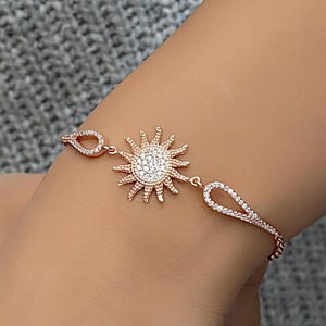Puede incluir: Una pulsera de oro rosa con un dije de sol. El dije de sol está incrustado con piedras de circonita cúbica transparentes.