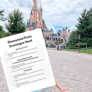 May include: A Disneyland Paris Scavenger Hunt sheet is held in front of Sleeping Beauty Castle. The castle is pink and blue with multiple turrets. The scavenger hunt includes tasks like finding a vintage vehicle and exploring the castle.