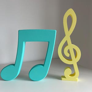 Può includere: Due decorazioni musicali in legno. Una è una chiave di violino blu turchese e l'altra è una nota musicale gialla.