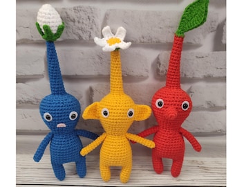 Puede incluir: Tres peluches de crochet con forma de personajes del videojuego 'Earthbound'. Las peluches son azules, amarillas y rojas, y cada una tiene un tocado único.