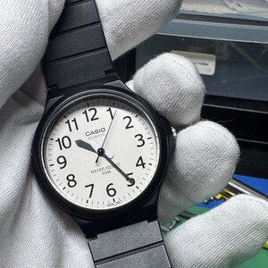 Peut inclure: Montre Casio Quartz noire avec un cadran blanc, des aiguilles noires et un bracelet noir. Le cadran affiche les chiffres de 1 &agrave; 12, avec le logo Casio et "WATER RESIST 50M" imprim&eacute; en dessous.