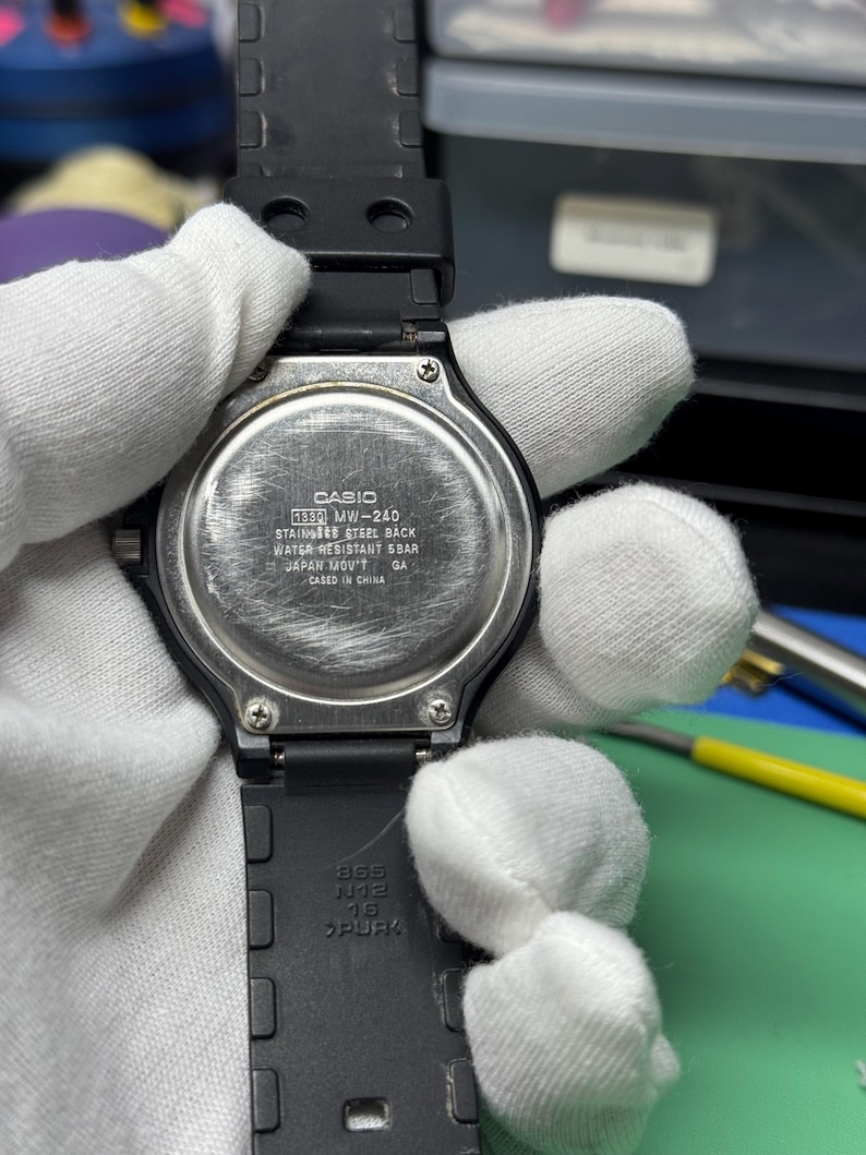 Peut inclure: Une montre Casio MW-240 noire avec un dos en acier inoxydable. La montre a un bracelet en caoutchouc noir et est r&eacute;sistante &agrave; l'eau. Le texte au dos indique "CASIO", "WATER RESISTANT 5BAR" et "JAPAN MOV'T".