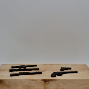 May include: Five black toy guns on a wooden surface. The guns are made of plastic and are about 3 inches long.