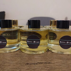 May include: Four clear glass bottles with black lids and labels that say "Bath Bliss" in white text. The bottles are filled with a light yellow liquid.