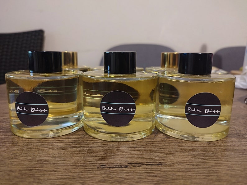 May include: Four clear glass bottles with black lids and labels that say "Bath Bliss" in white text. The bottles are filled with a light yellow liquid.