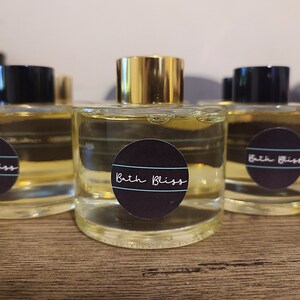 May include: Three clear glass bottles with gold lids and black labels that say "Bath Bliss". The bottles are filled with a light yellow liquid.