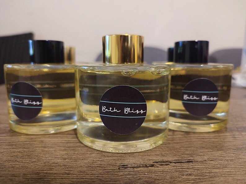 May include: Three clear glass bottles with gold lids and black labels that say "Bath Bliss". The bottles are filled with a light yellow liquid.