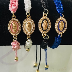 May include: Four braided bracelets with a gold oval charm featuring a religious figure. The bracelets are pink, white, black, and blue.