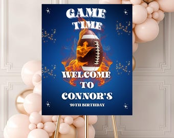 May include: A welcome sign for Connor's 10th birthday, featuring a football engulfed in flames against a blue background. The sign reads "Game Time" and "Welcome to Connor's". The sign is displayed on a gold easel, with balloons in the background.