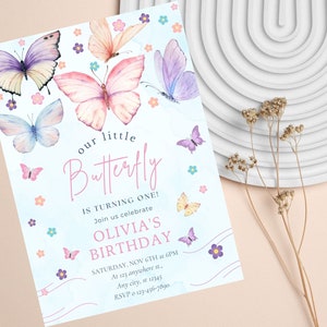 Puede incluir: Una invitaci&oacute;n azul y blanca con un dise&ntilde;o de mariposa de acuarela. El texto dice "nuestro peque&ntilde;o Butterfly est&aacute; cumpliendo un a&ntilde;o! &Uacute;nase a nosotros para celebrar el cumplea&ntilde;os de Olivia. S&aacute;bado, 6 de noviembre a las 6 pm. En 123 anywhere st. Any city, st 12345. RSVP 123-456-7890"
