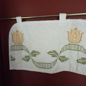 May include: White valance with embroidered floral design. The valance features two yellow tulip-like flowers and green leaf patterns. The fabric is attached to the rod with white loops.