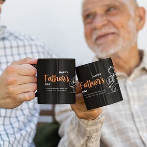 May include: Two black mugs with white handles. The mugs have the text "Happy Father's Day" in orange lettering and a small illustration of a person holding a mug.
