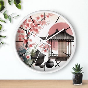 Peut inclure: Horloge ronde blanche avec des aiguilles noires et un motif floral rose et blanc. L'horloge présente une illustration en noir et blanc d'un bâtiment de style japonais avec un toit rouge et un soleil rouge en arrière-plan. On y trouve également des illustrations en noir et blanc de théières et de tasses à thé.