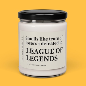Peut inclure: Bougie en cire de soja blanche dans un pot en verre avec un couvercle noir. L'étiquette indique "Smells like tears of losers I defeated in LEAGUE OF LEGENDS." La bougie est de 255 grammes.