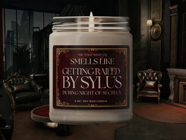 May include: A white soy wax candle in a glass jar with a silver lid. The label reads "SMELLS LIKE GETTING RAILED BY SYLUS" with the text "DURING NIGHT OF SECRECY" below. The candle is 9 oz.