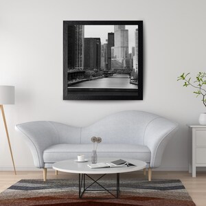 Könnte beinhalten: Schwarz-weiß gerahmte Fotografie einer Stadtlandschaft. Das Bild zeigt hohe Gebäude, einen Fluss und eine Brücke. Das Foto wird über einem hellgrauen Sofa, einem runden Couchtisch und einem gestreiften Teppich angezeigt.