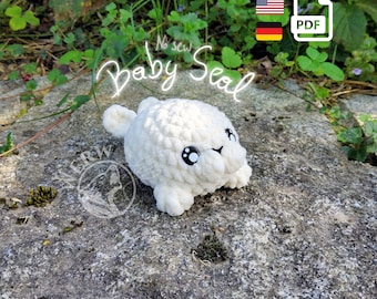 May include: A white crocheted baby seal plush toy with black eyes. The toy is sitting on a gray rock with green plants in the background. The text "No sew Baby Seal" is written above the toy.