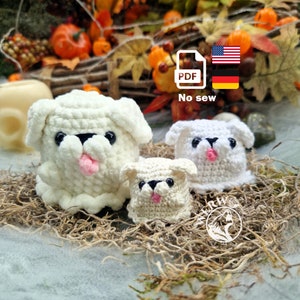 May include: Three white crocheted dog amigurumi toys, with black eyes and pink tongues, sitting on a bed of brown moss. The largest dog is in the center, with a smaller dog on either side. The image includes the text "No sew" and a PDF icon.
