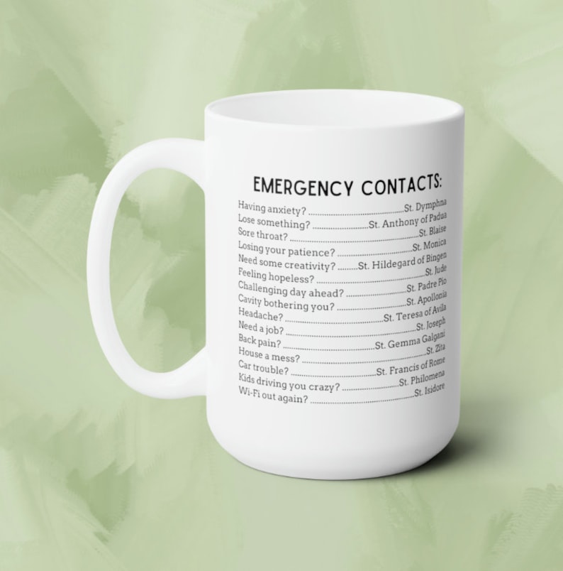 May include: White ceramic coffee mug with a black text design that reads "Emergency Contacts" and lists various situations with a corresponding saint to call upon for help.
