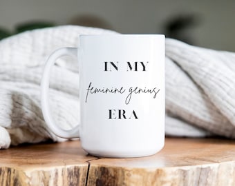 May include: White ceramic mug with a black inscription that reads "In my feminine genius ERA".