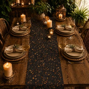 May include: A dark navy blue table runner with a small-scale floral pattern in shades of orange, yellow, and brown, centered on a rustic wooden dining table set with plates, linen napkins, wine glasses, and several lit pillar candles.