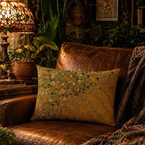 Peut inclure: Un coussin rectangulaire présentant un fond jaune moutarde avec un motif dense et dispersé de petits éléments floraux circulaires dans des tons de vert, d'or et de brun foncé, posé sur un fauteuil en cuir marron à la surface texturée.