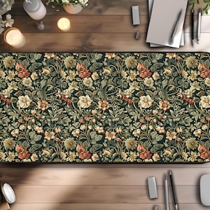 Puede incluir: Una alfombrilla de escritorio rectangular con un detallado estampado floral en tonos verdes, crema y naranja. El diseño incluye varias flores y follaje sobre un fondo oscuro. La alfombrilla está sobre una superficie de madera.